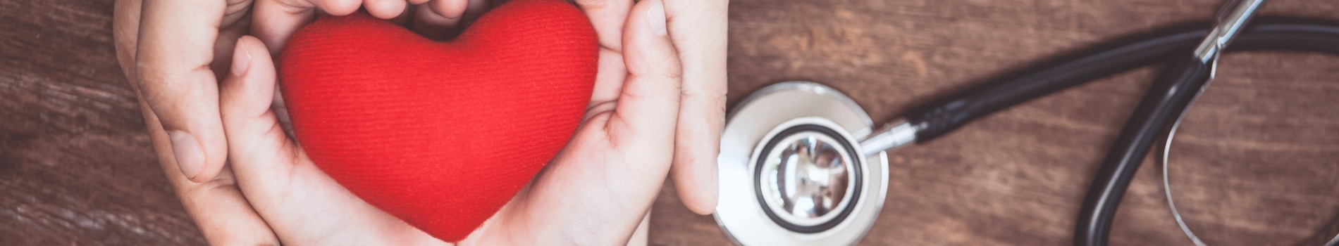 Red heart held in hands of woman and child with doctors stethoscope.